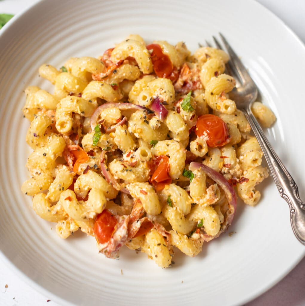 Baked Feta pasta with cherry tomatoes and basil on white plate with a fork