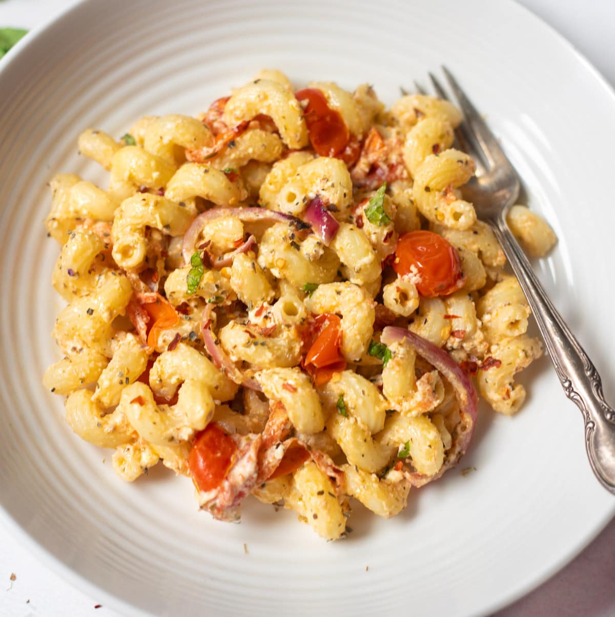 Baked Feta pasta with cherry tomatoes and basil on white plate with a fork