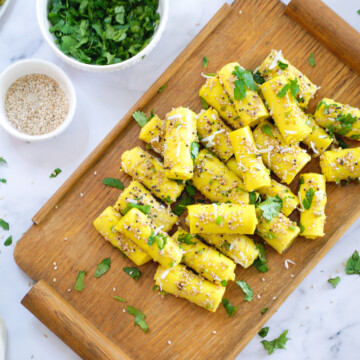 Gujarati Khandvi on a serving tray with sesame seeds and cilantro on the side