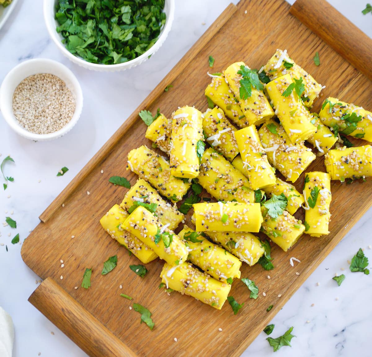 Gujarati Khandvi on a serving tray with sesame seeds and cilantro on the side
