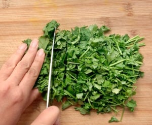 Cutting cilantro leaves with a sharp knife on a wooden cutting board