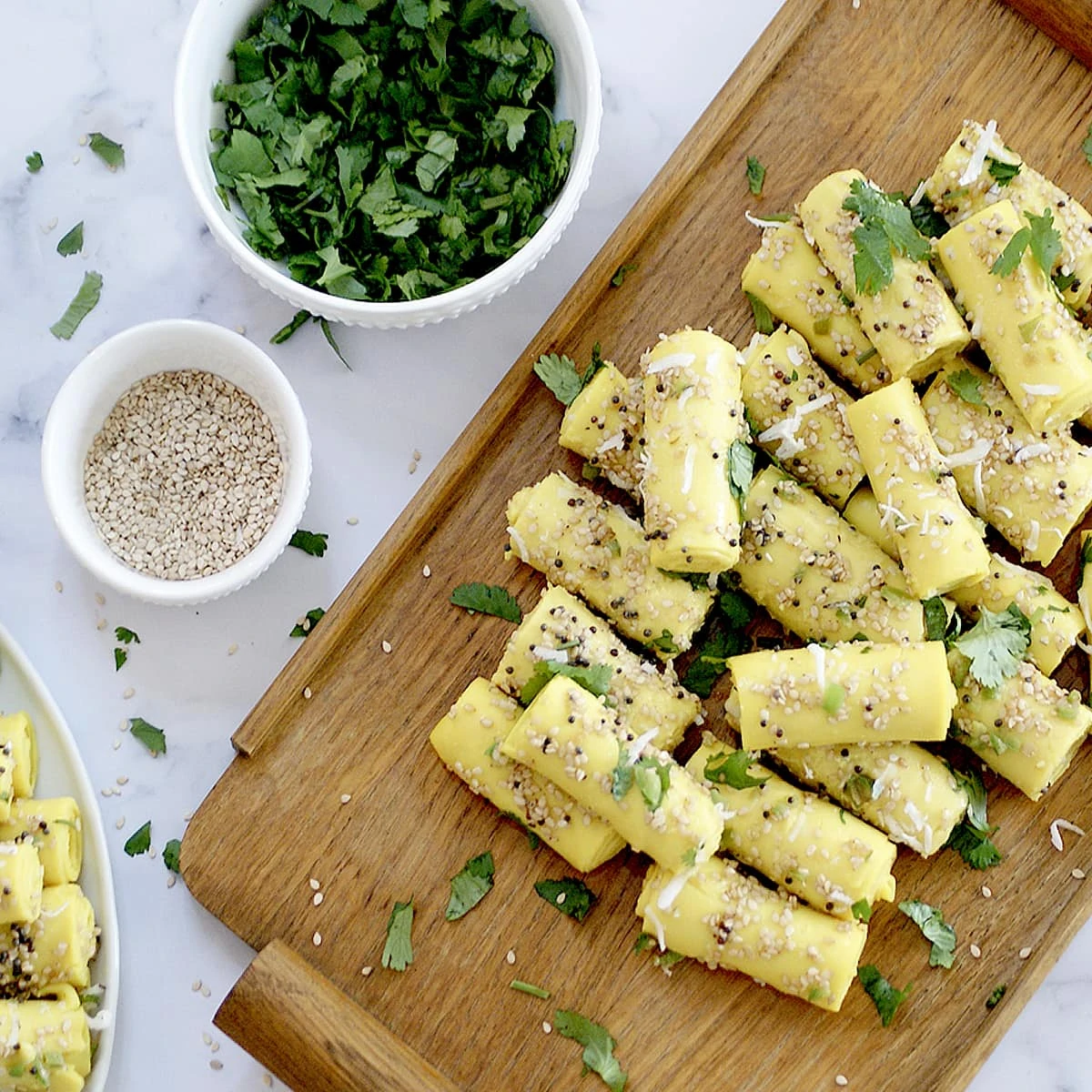 Gujarati Khandvi in a wooden board garnished with cilantro and sesame seeds