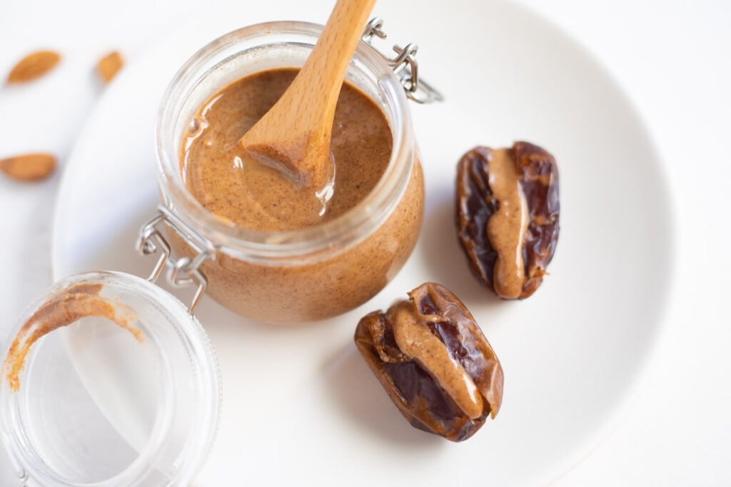 homemade almond butter in glass jar on white plate with dates