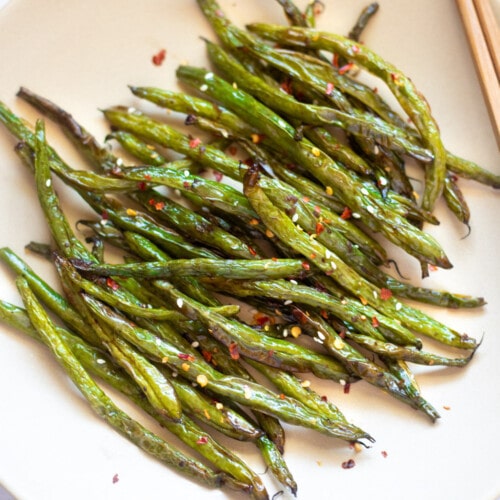 roasted garlic green beans asian style in a plate topped with sesame seeds and red pepper flakes