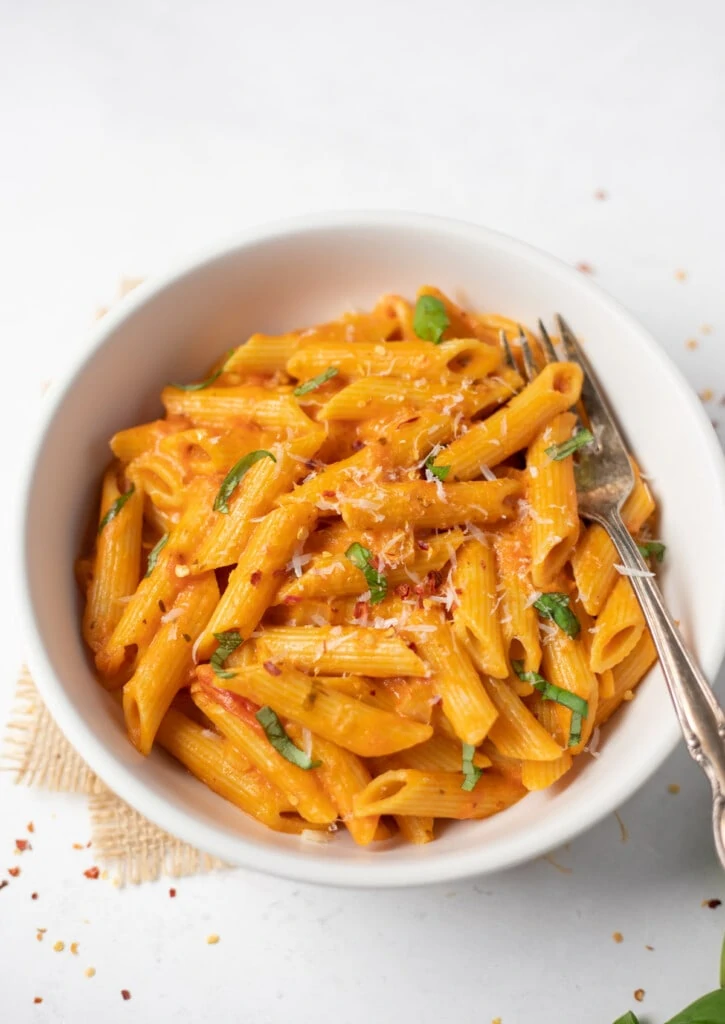 Creamy homemade penne pasta in a white bowl garnished with basil and parmesan