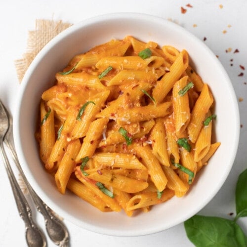 Creamy penne alla vodka pasta in a white bowl garnished with basil and parmesan
