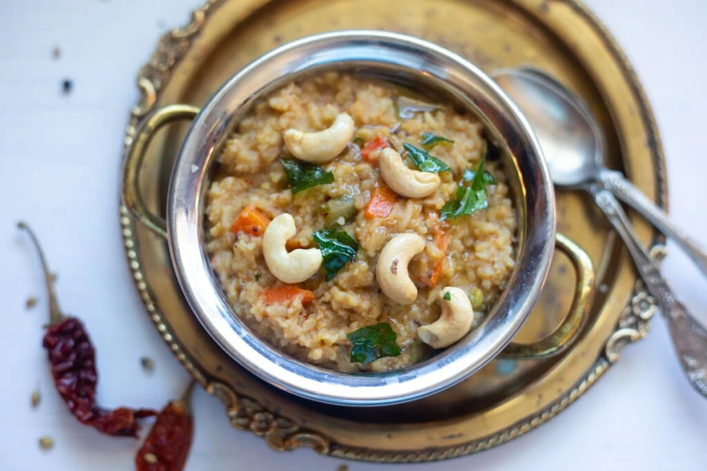 Bisi Bele Bath with means hot lentil rice in a bowl topped with cashews and tempering