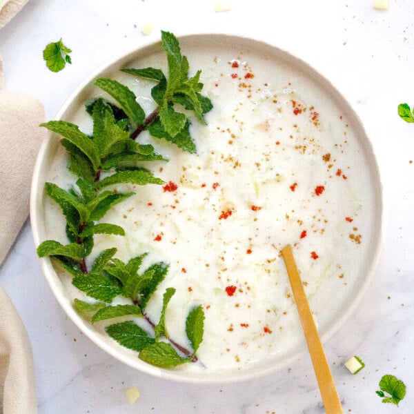 Cucumber Raita in a bowl garnished with mint leaves and spices