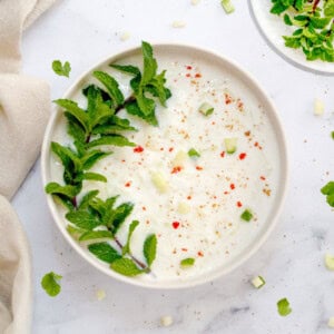 Cucumber Raita in a bowl garnished with mint leaves and spices