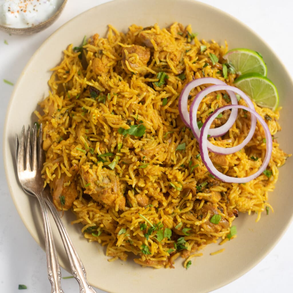 chicken biryani served on a plate garnished with cilantro, onions and lime