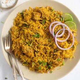 chicken biryani served on a plate garnished with cilantro, onions and lime