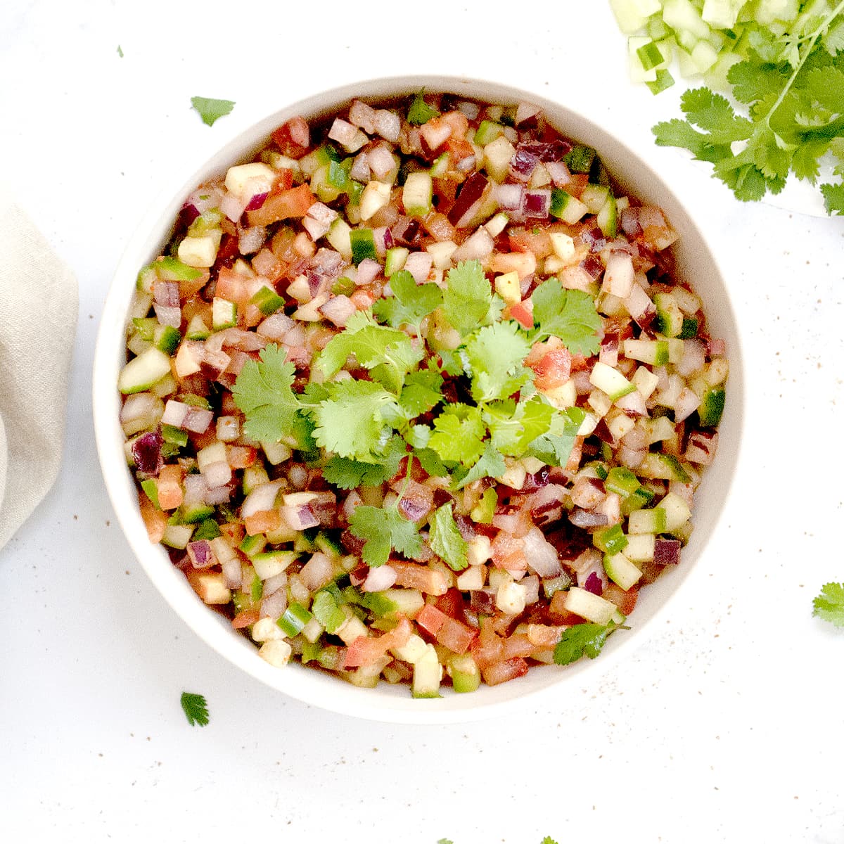 Kachumber salad made with onions, tomatoes and cucumber in a bowl garnished with cilantro leaves. 