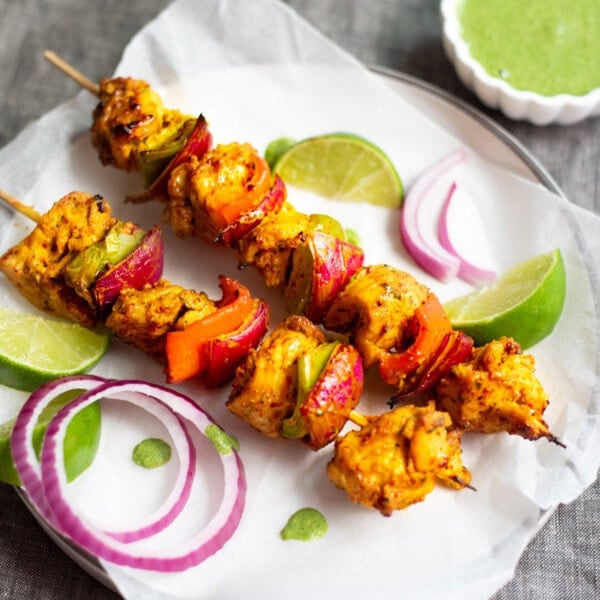 Chicken Tikka Kebab skewers served on a plate with chutney, red onions and lime.