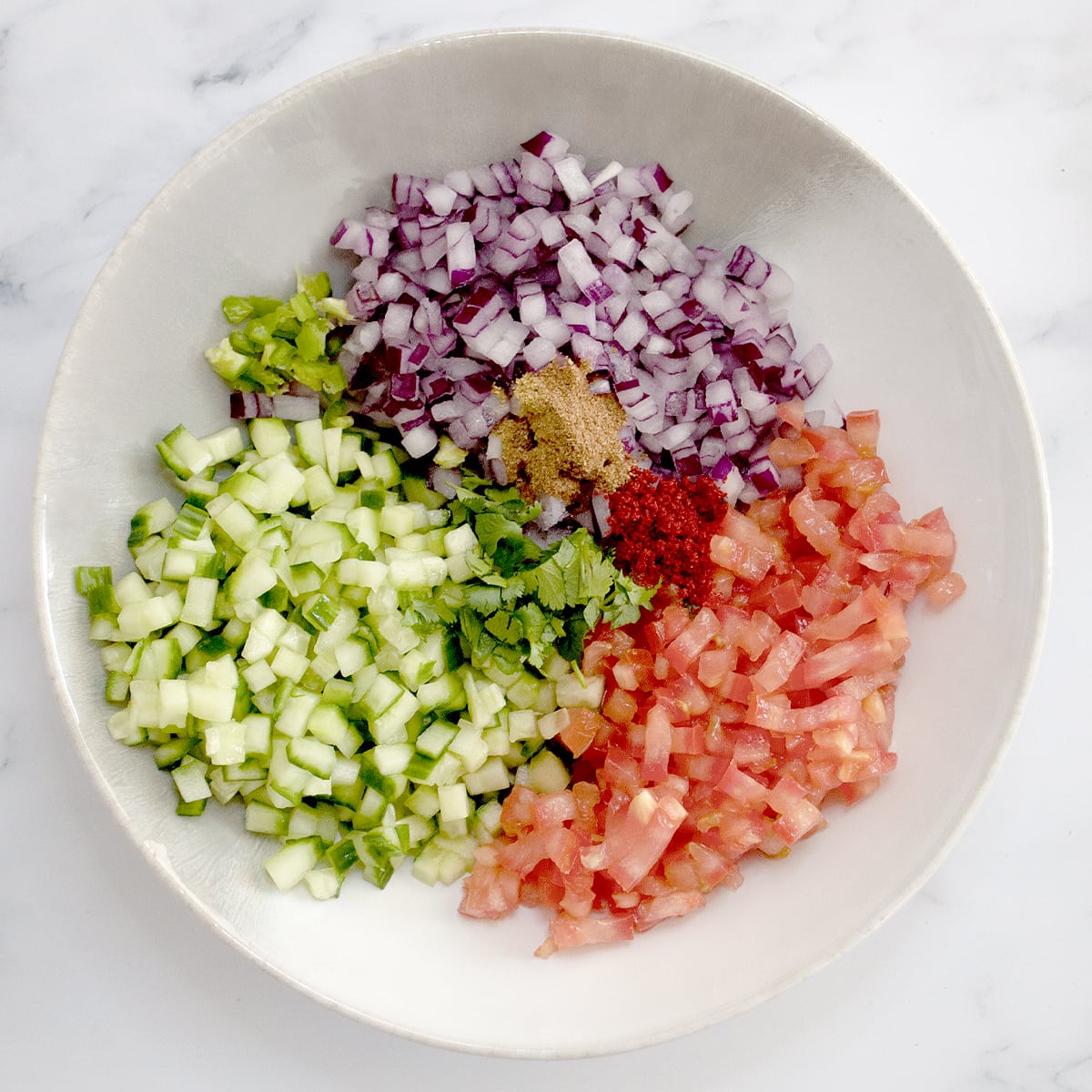 kachumber salad ingredients such as cucumber, tomato, onion and spices in a white bowl