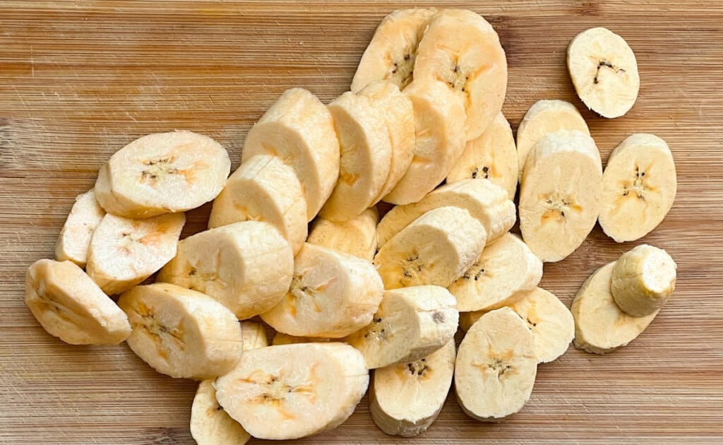 Raw sliced plantains on a wooden cutting board