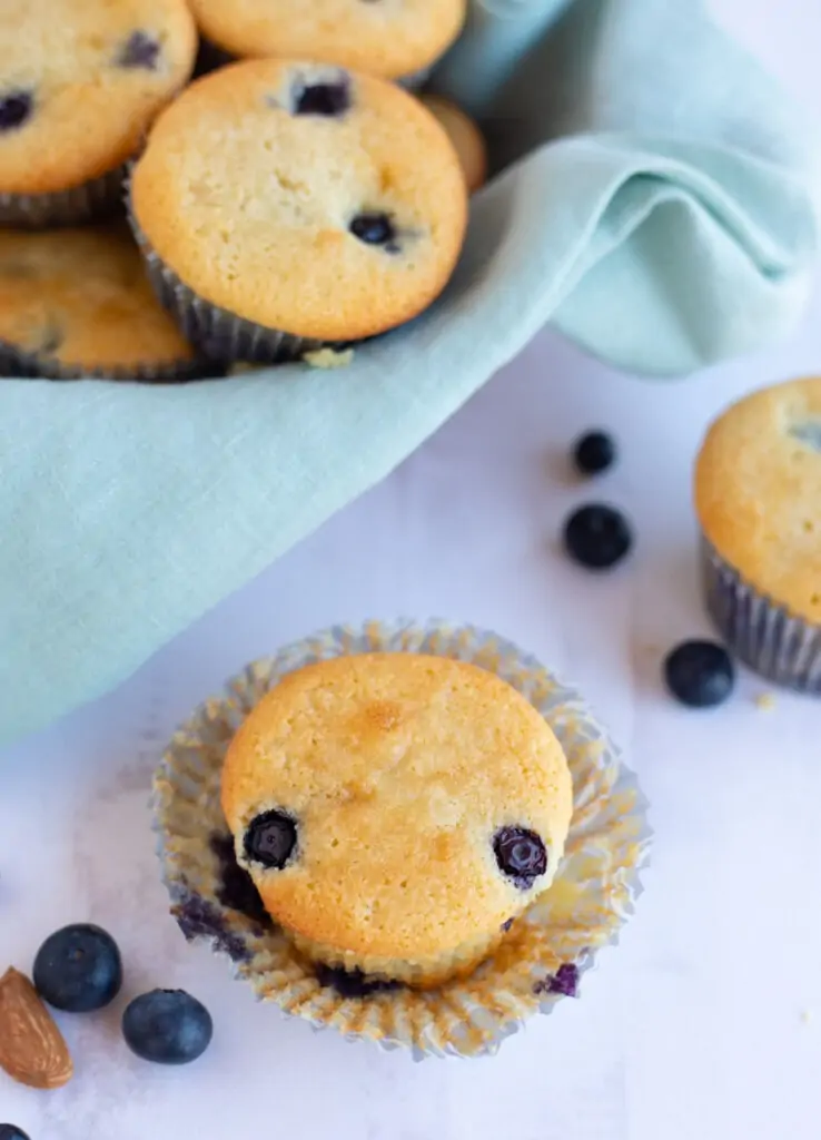 Light and moist blueberry muffin on a white table with more muffins in a basket