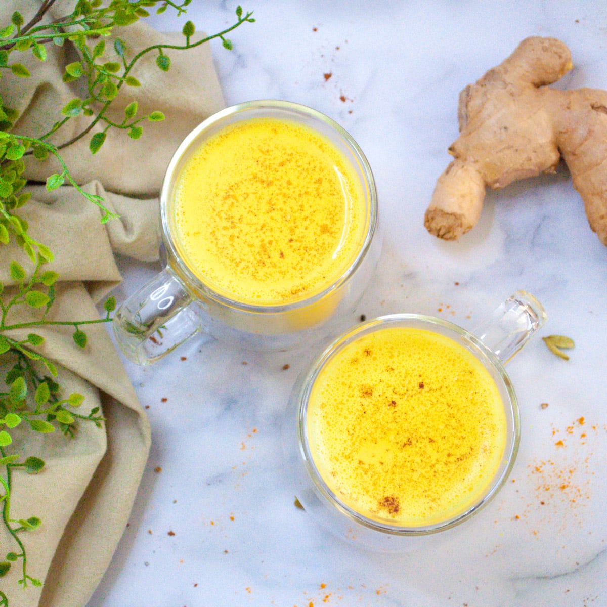Turmeric milk (Haldi doodh) in two cups along with ginger on the side
