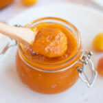 Apricot jam being taken out by a spoon from a glass jar