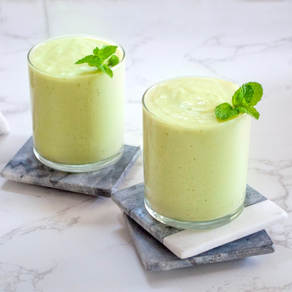 avocado banana smoothie garnished with mint leaves in 2 glasses