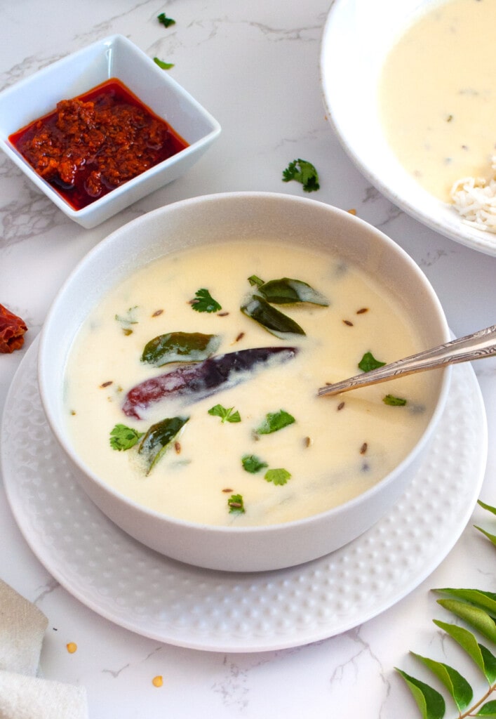 Gujarati Kadhi in a bowl garnished with cilantro and pickle on the side