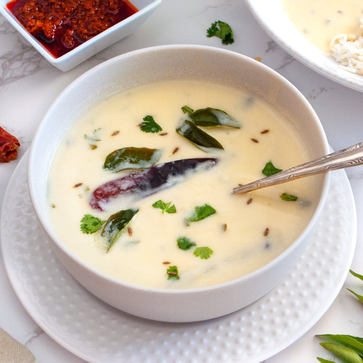 Gujarati Kadhi in a bowl garnished with cilantro and pickle on the side