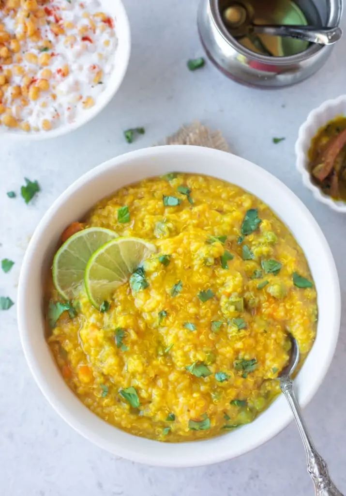 Delicious quinoa Khichdi in a bowl garnished with cilantro and lime, with ghee, pickle and yogurt on the side.