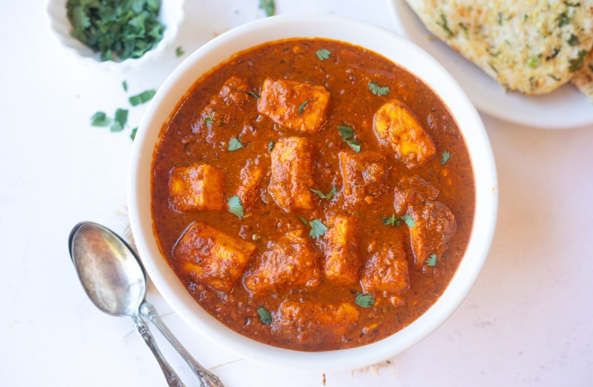 Paneer vindaloo curry in a bowl served with naan as a side