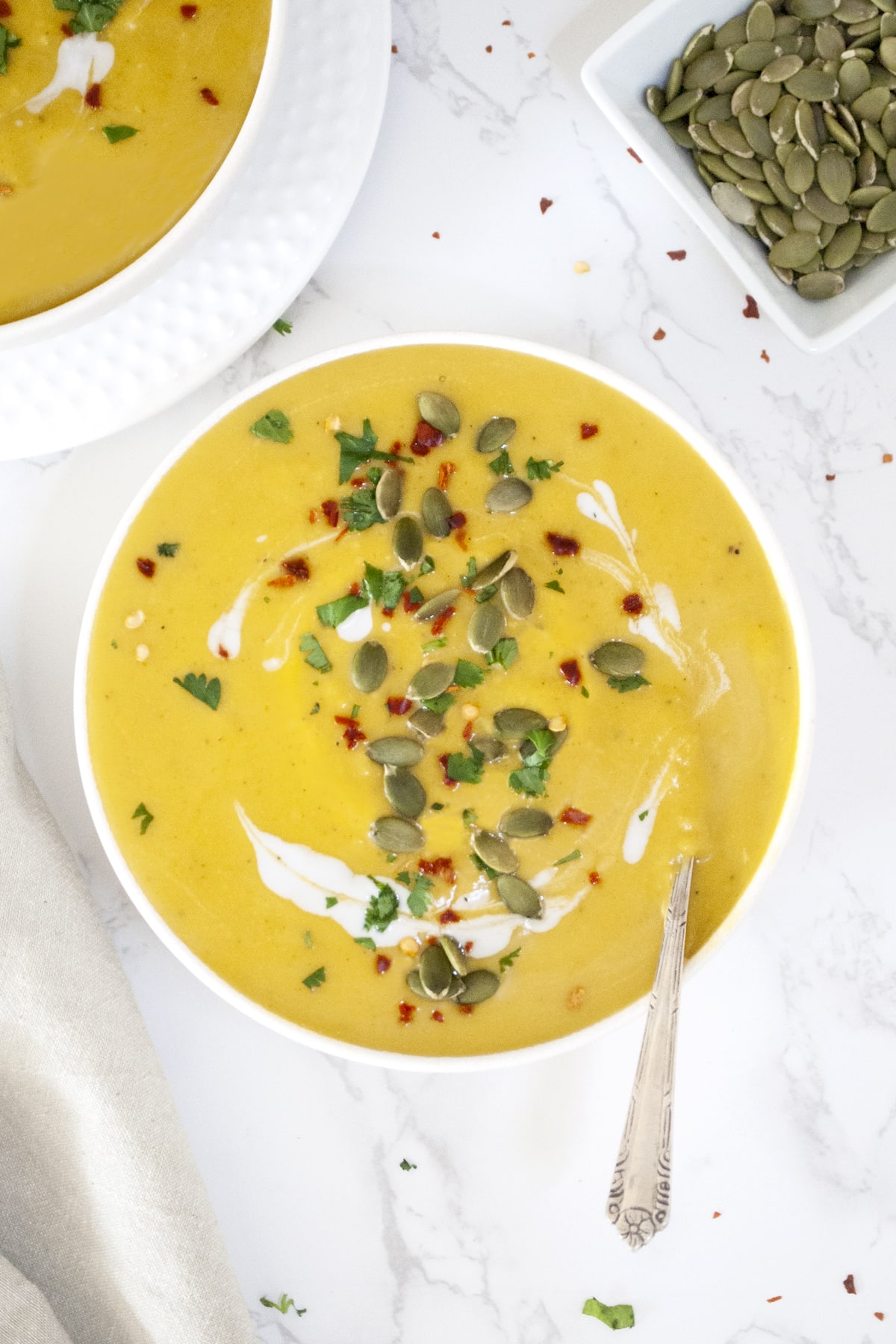 Creamy Vegan Curried Pumpkin Soup garnished with pumpkin seeds, cilantro and red chili flakes