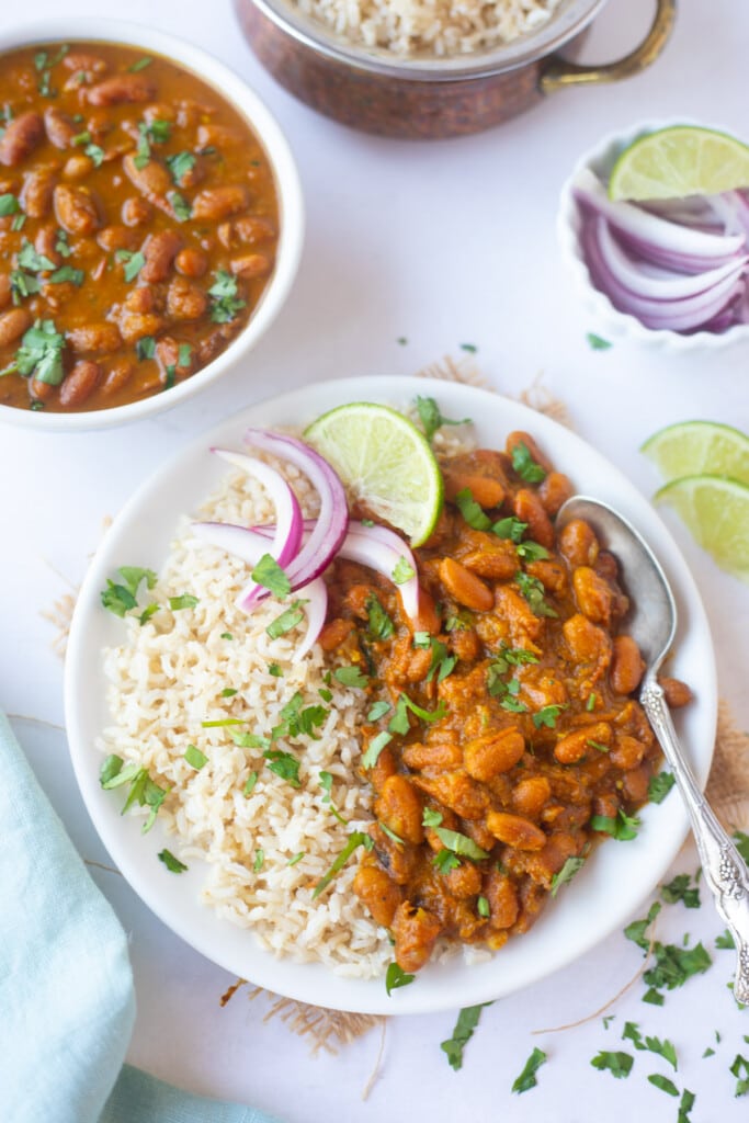 Kidney beans curry with rice (rajma chawal) in a plate garnished with cilantro, lime and onions 