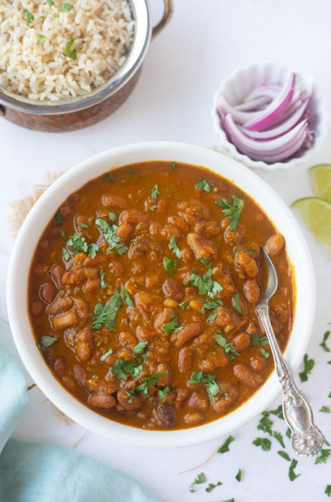 Rajma Masala in a bowl garnished with cilantro and rice and onions on the side 