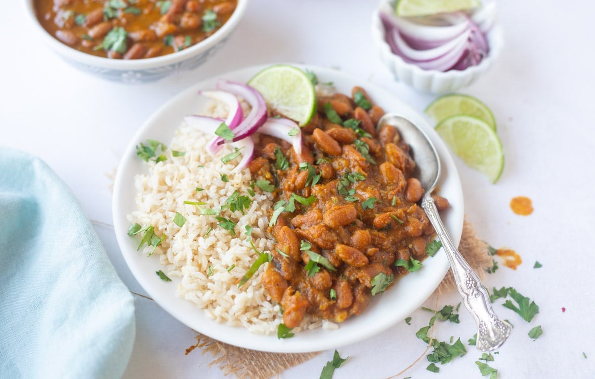 Rajma chawal (red beans with rice) in a plate garnished with cilantro, lime and onions