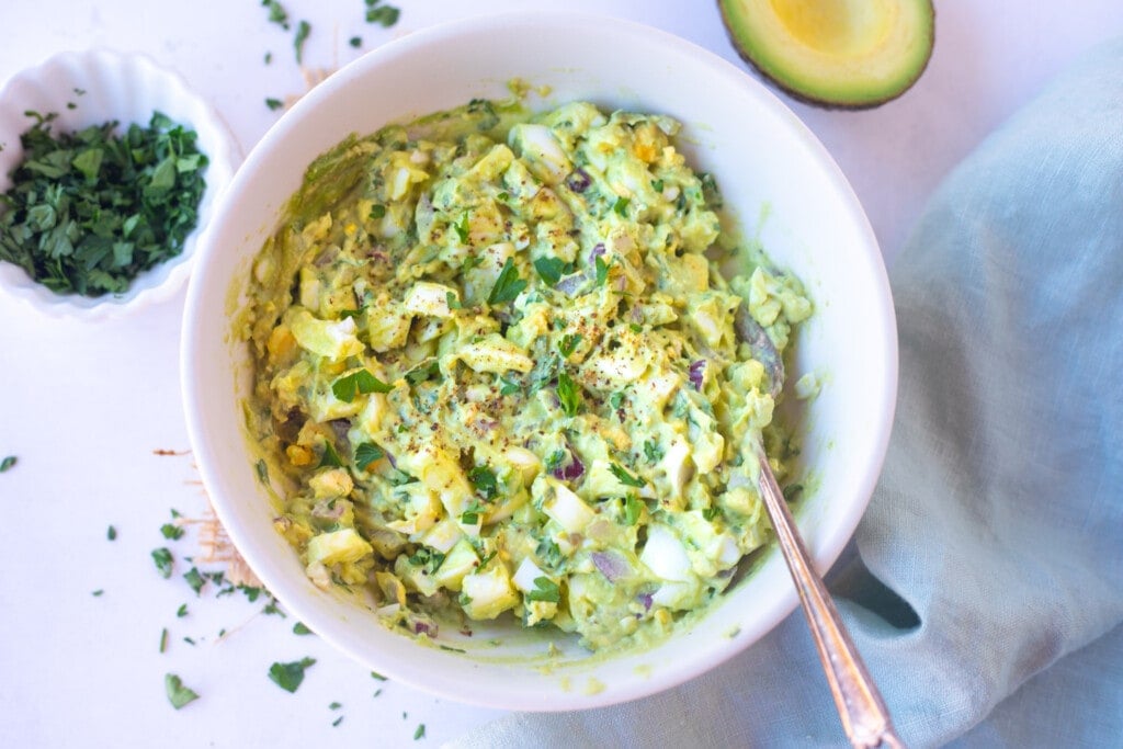 Avocado egg salad in a bowl topped with chopped parsley 