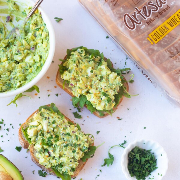 Avocado egg salad sandwich on a whole wheat bread topped with arugula
