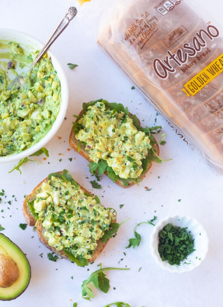 Avocado egg salad sandwich on a whole wheat bread topped with arugula