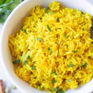 indian turmeric yellow rice in a bowl garnished with cilantro leaves