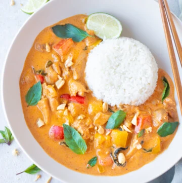 Panang Curry with chicken served in a bowl with jasmine rice and garnished with thai basil leaves