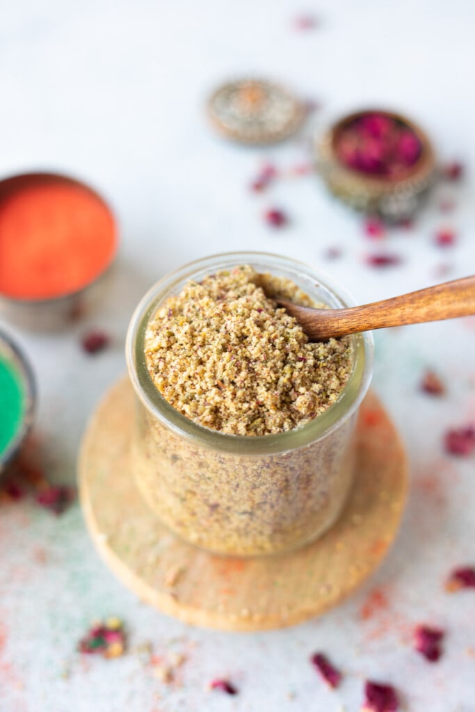 Thandai Powder in a pretty jar with rose petals and holi colors on the side 