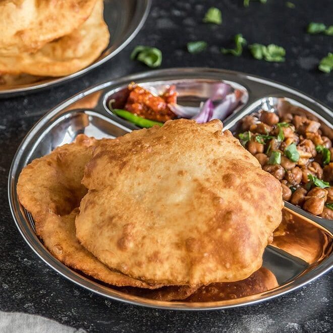 Bhature served with chole, onion and pickle on a steel thali