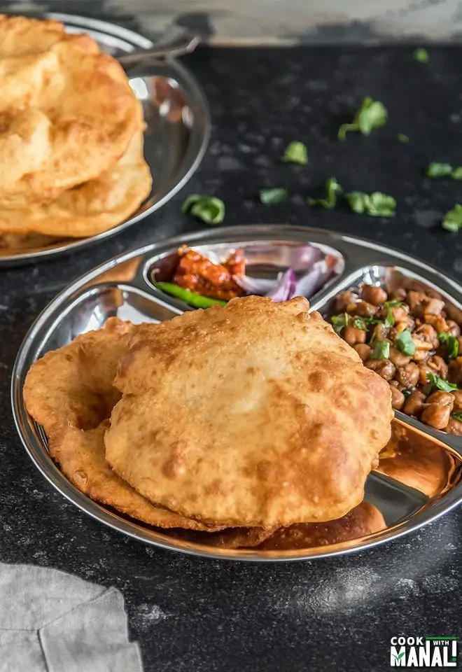 Bhature served with chole, onion and pickle on a steel thali