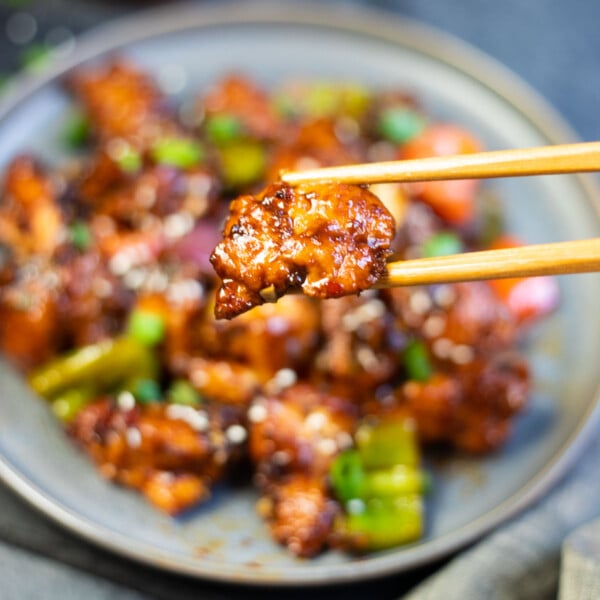Crispy Chilli Chicken in chopsticks over a full plate.