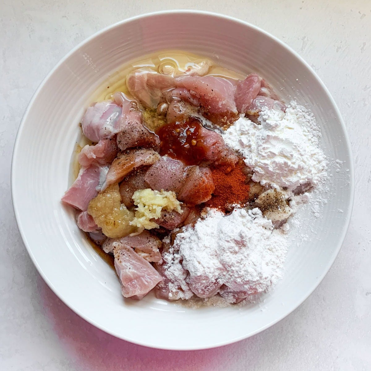 Marinate chicken to make chilli chicken in a white bowl 