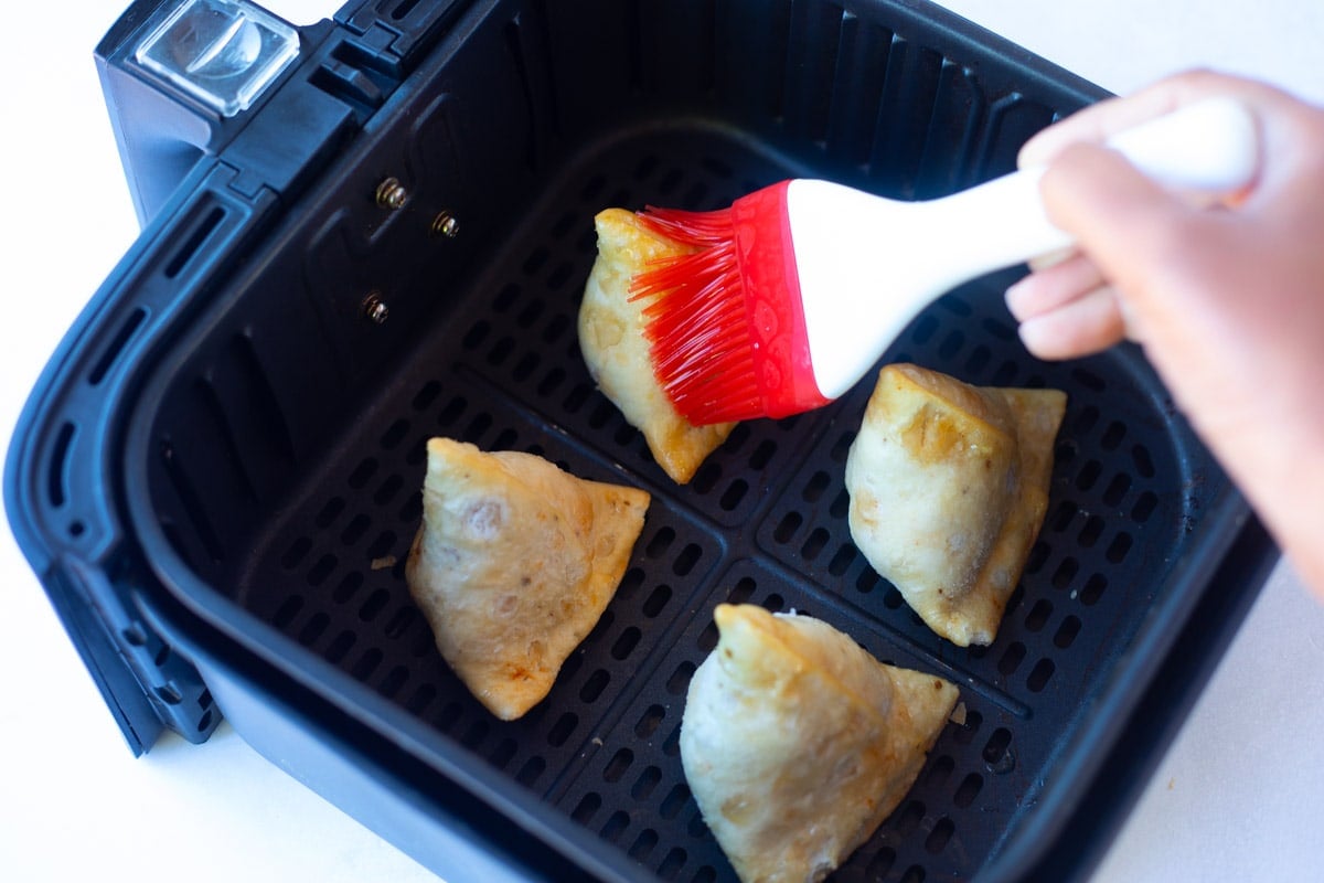 Brushing oil on frozen samosa to be cooked in the air fryer 