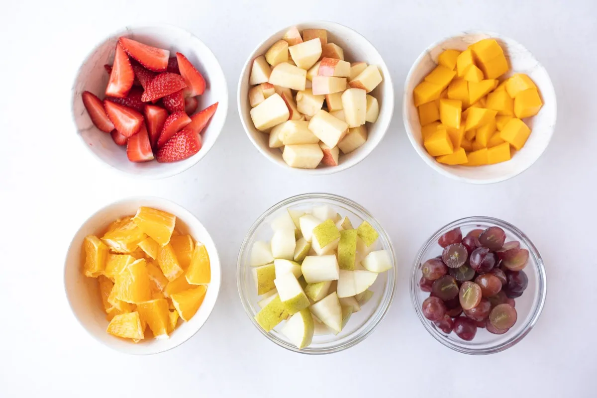 Cut up fruits to make fruit salad in small bowls 