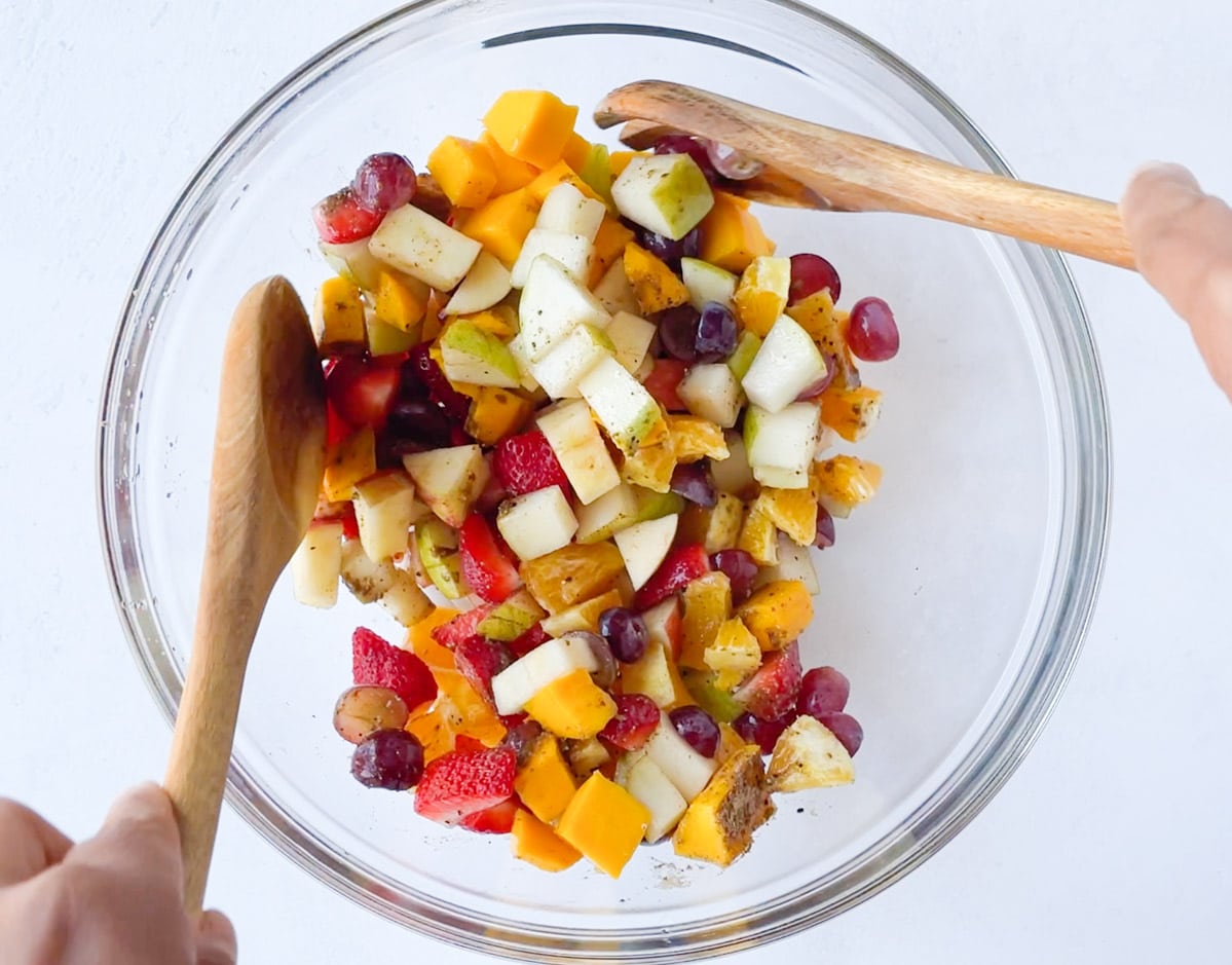 Tossing the fruits with seasoning to make Pakistani fruit salad