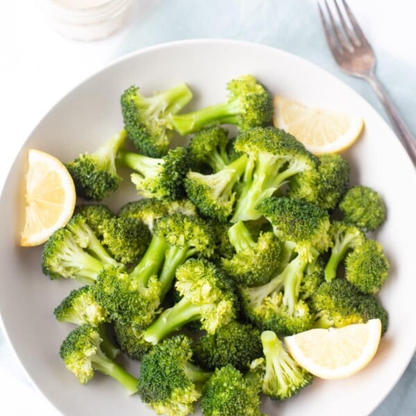 steamed broccoli in a bowl served with lemon wedges and tahini dip