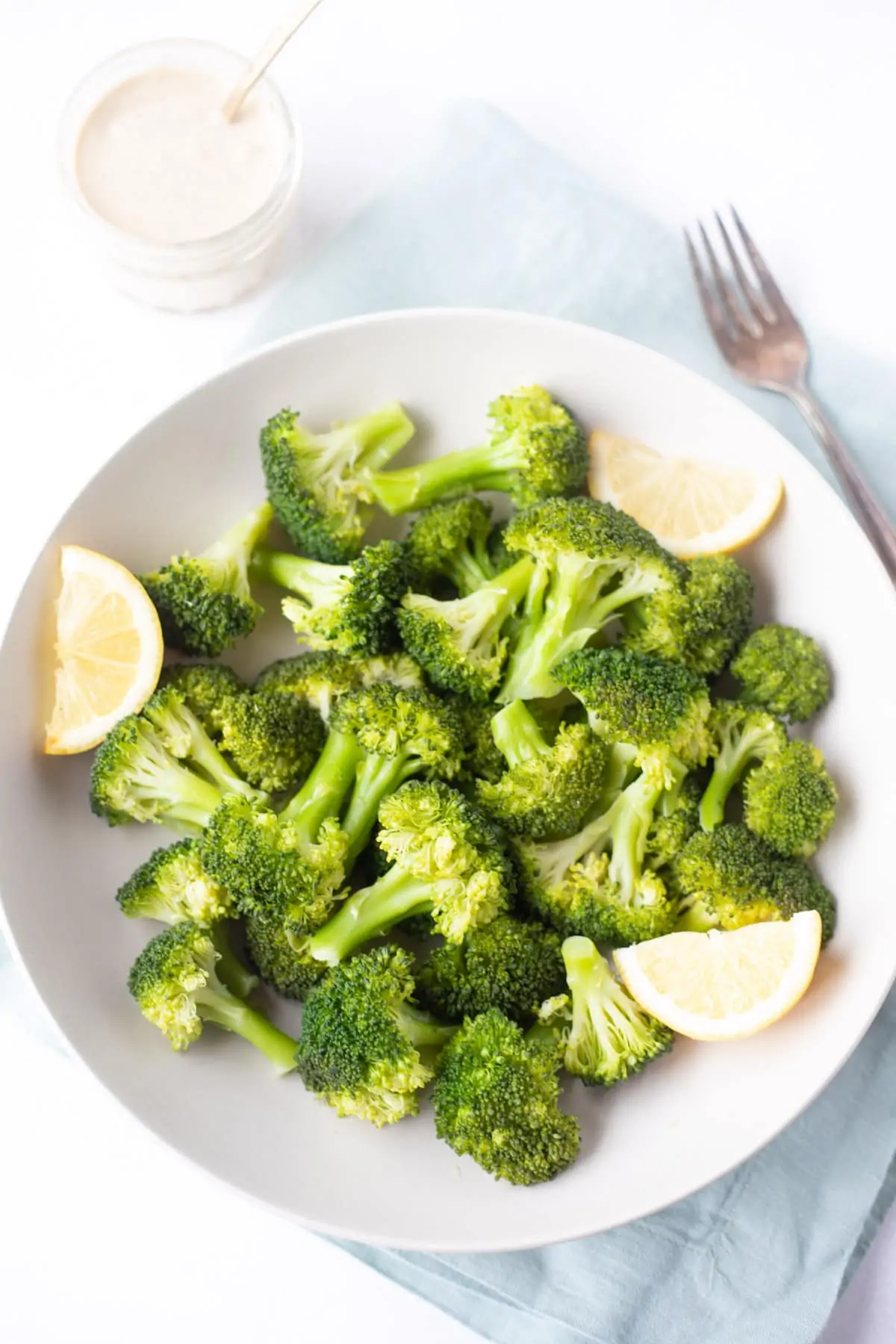 steamed broccoli in a bowl served with lemon wedges and tahini dip