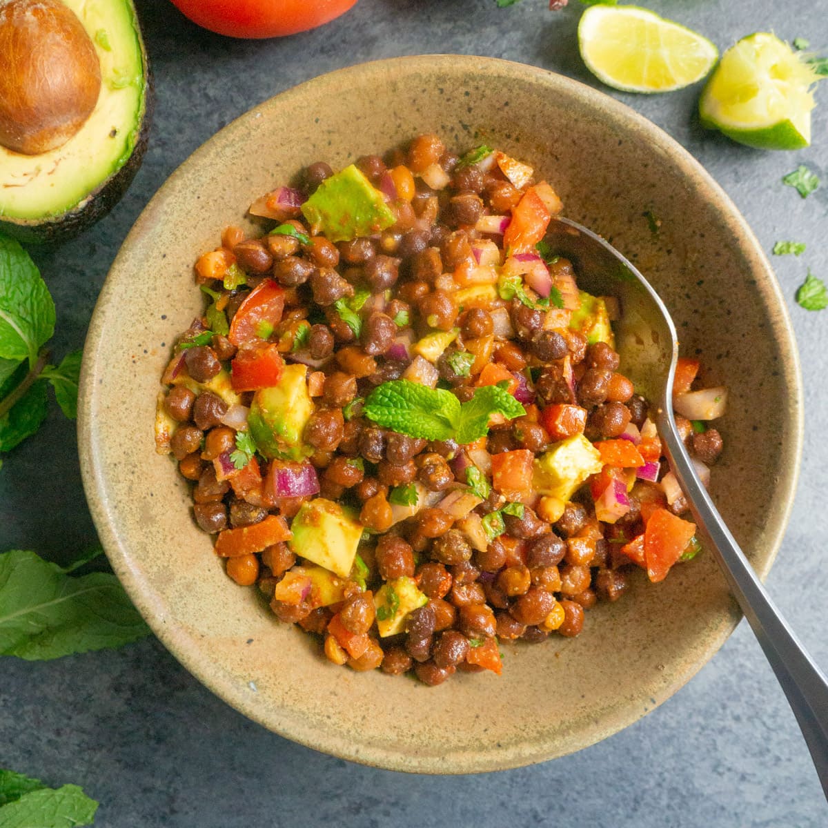 Kala Chana Chaat. Black Chickpea Salad in a bowl with avocado, tomato, onion, mint and lime pieces