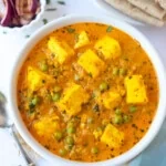 Creamy Matar Paneer served in a bowl with roti and onions on the side