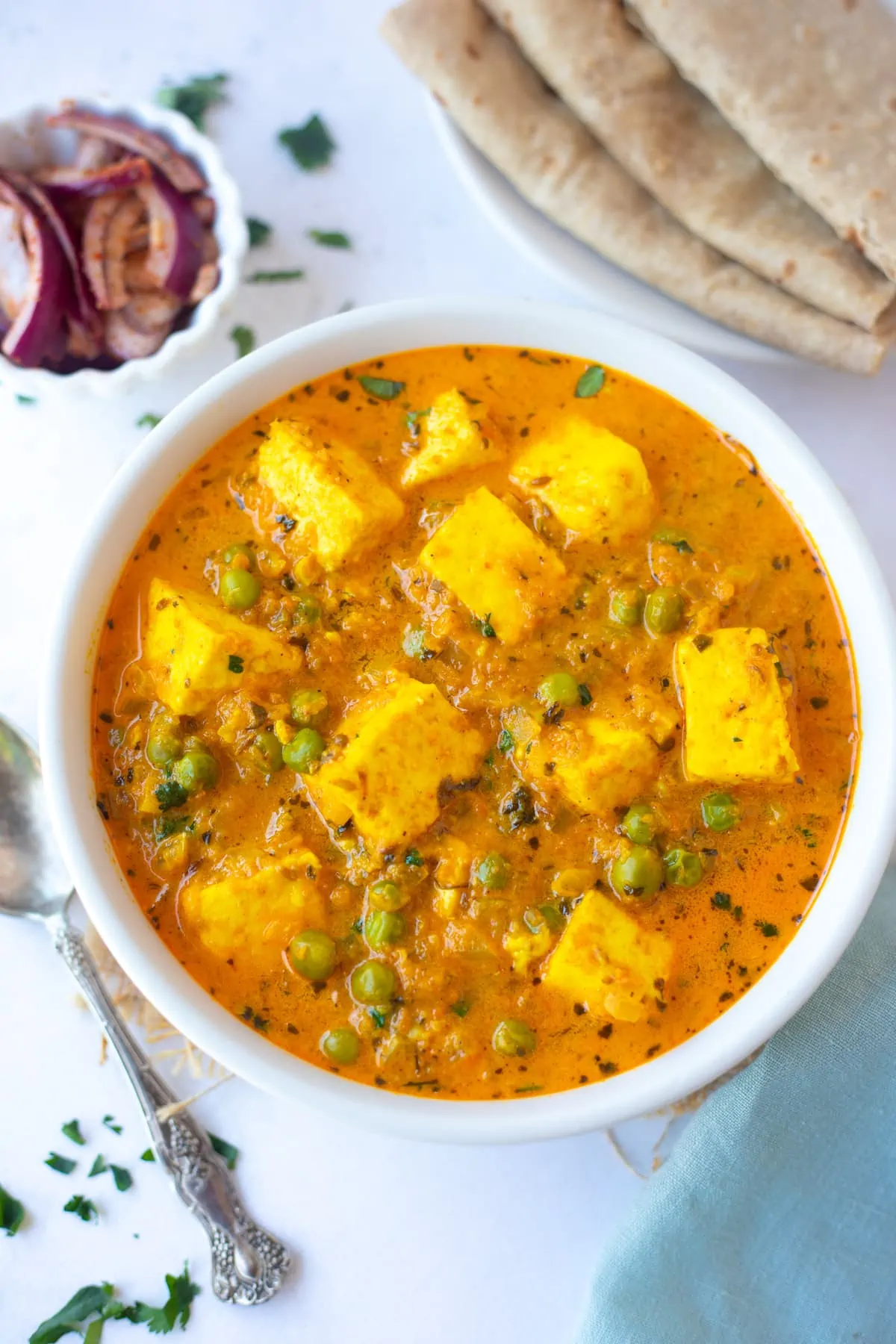 Creamy Matar Paneer served in a bowl with roti and onions on the side 