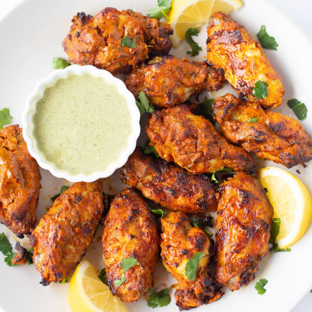 Indian style Tandoori chicken wings served in a platter with a dip and lemon wedges